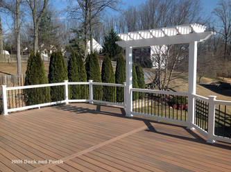 Vinyl deck using Wolf Tropical Hardwoods Collection PVC Decking with Amberwood flooring, white PVC railing, black round aluminum balusters by Longevity, and a white pergola.